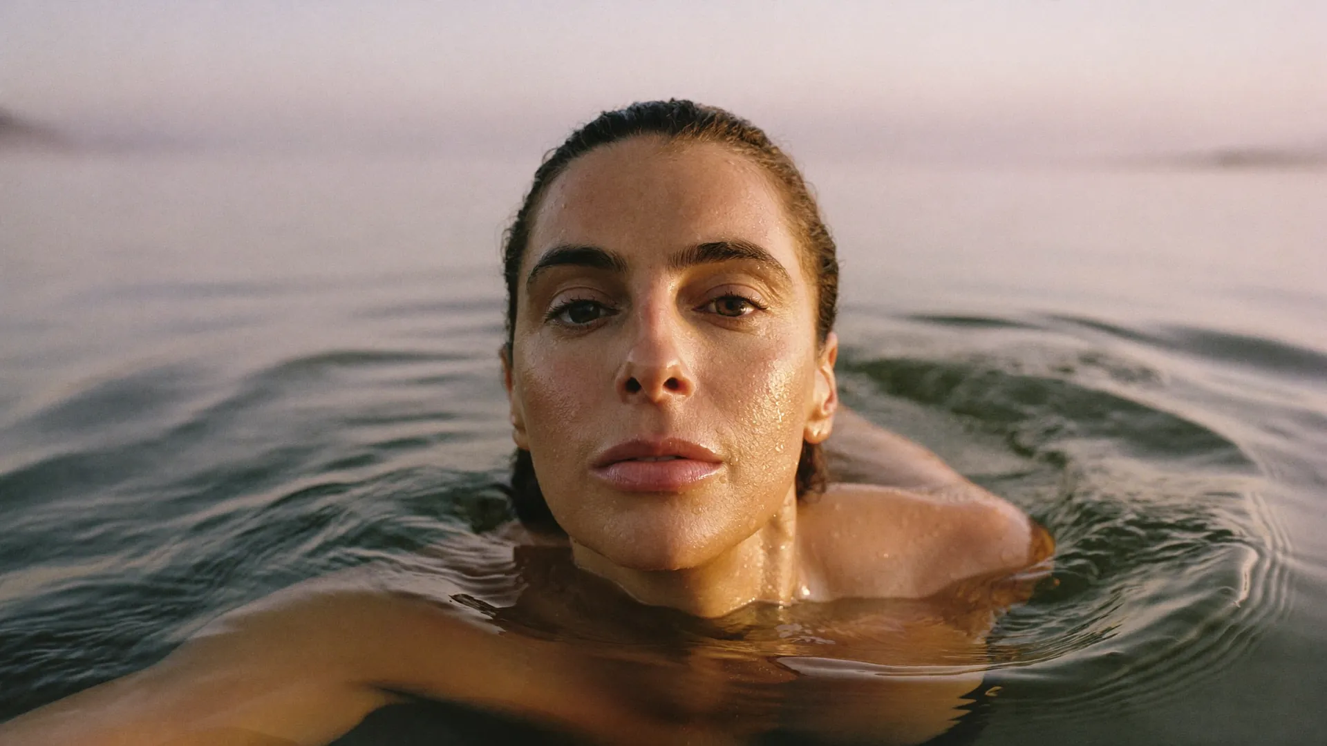 Eine Frau schwimmt im Morgengrauen im stillen See, Wassertropfen glänzen auf ihrer Haut.