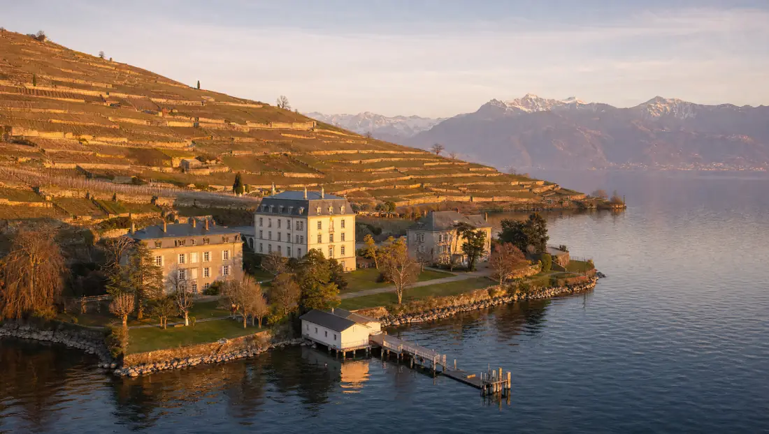 The lake campus at golden hour: the manor, two boarding houses, the boathouse and the jetty below the Lavaux vineyards