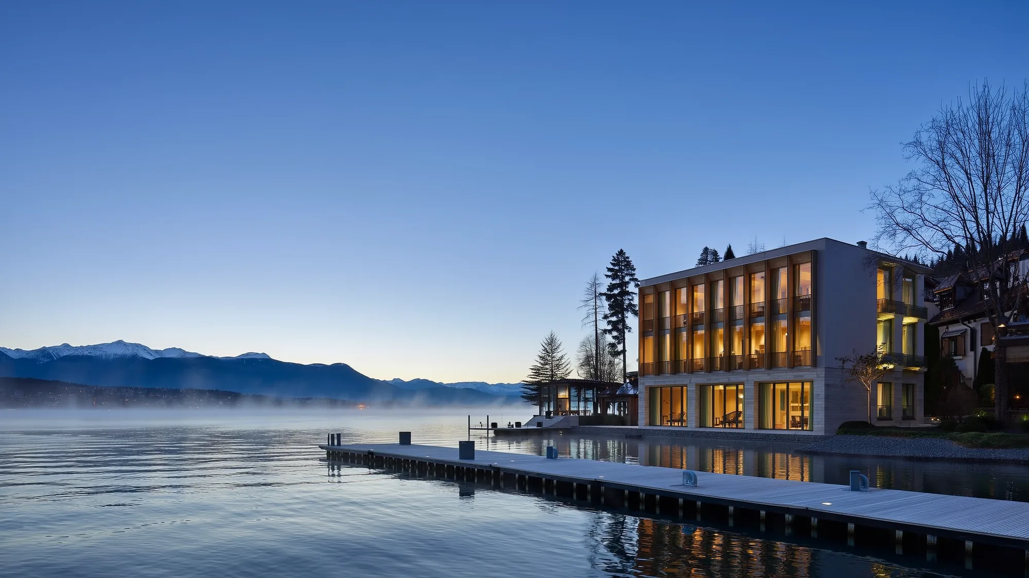 A clinic building beside a Swiss lake at dawn, its windows lit.