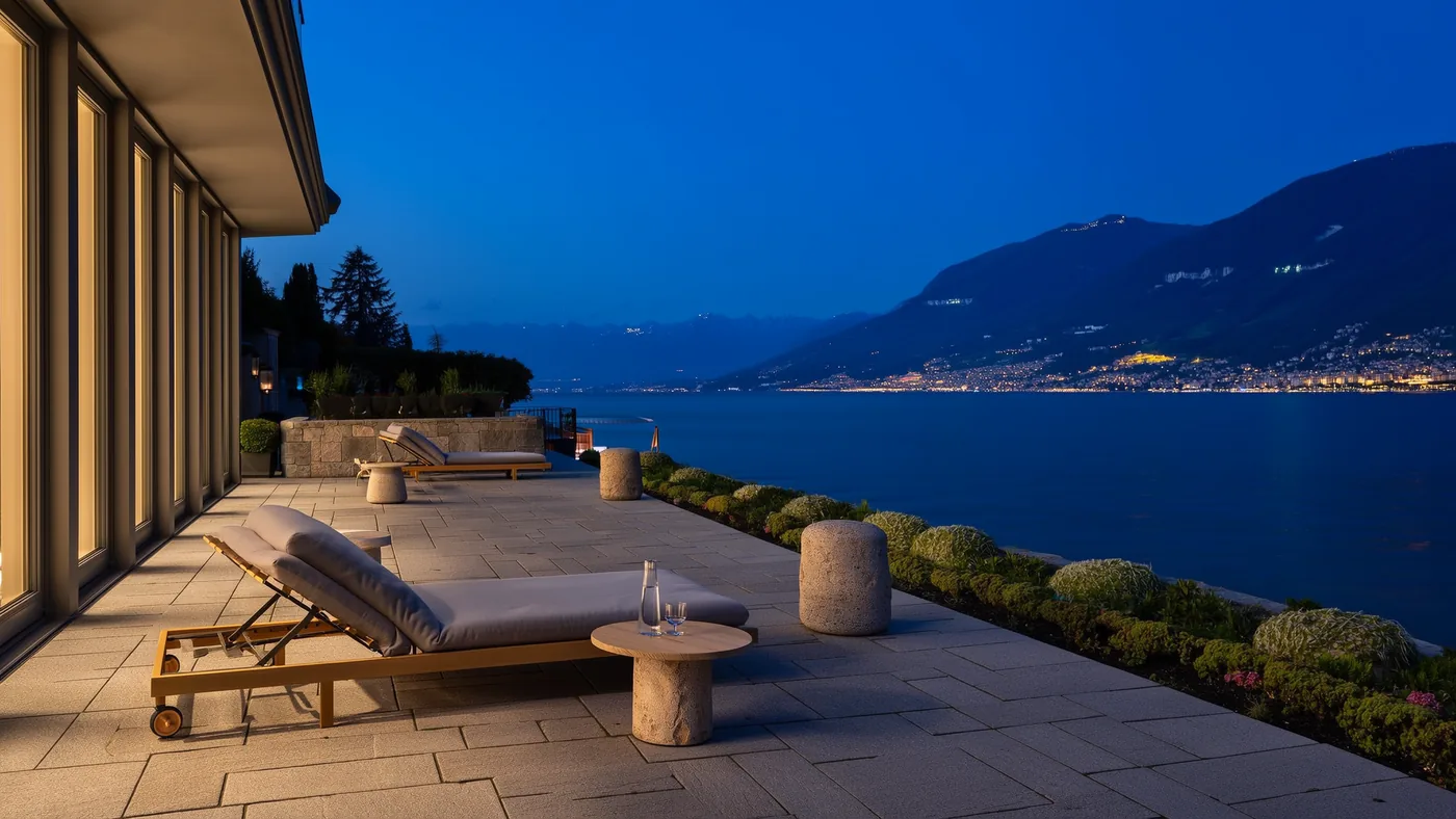 A stone terrace with loungers above a Swiss lake at dusk.